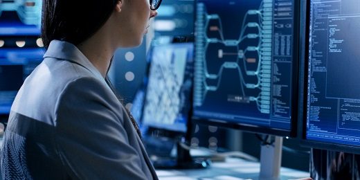 Female System Engineer Controls Operational Proceedings. In the Background Working Monitors Show Various Information.